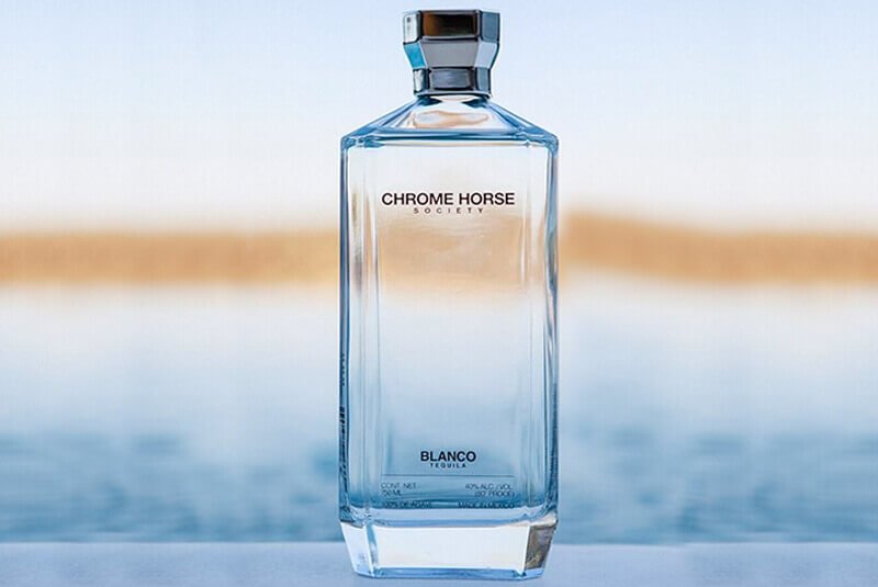 Chrome Horse Society blanco tequila bottle against a blurred sea view