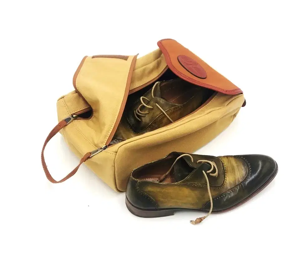 Tan canvas shoe bag with leather trim and a zip opening, holding a pair of brogues